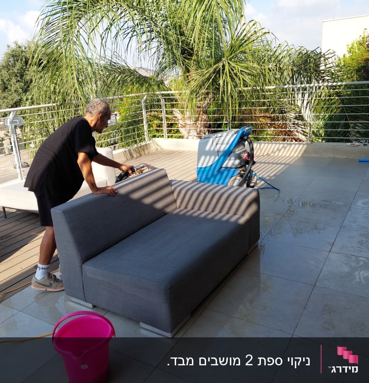 אדם מנקה ספה עם מכשיר ניקוי על מרפסת